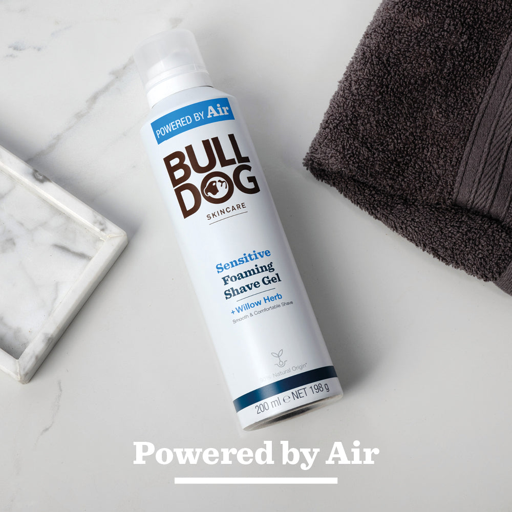 A can of Sensitive Foaming Shave Gel, ideal for sensitive skin, sits on a marble tray next to a folded dark gray towel on a light surface, with “Powered by Air” displayed at the bottom.
