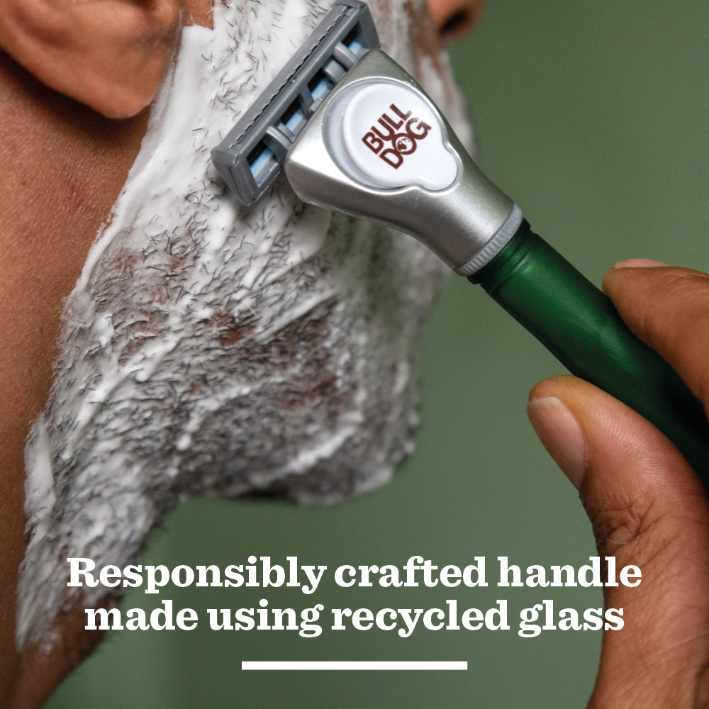 A person shaves their foamy cheek with the Original Glass Razor’s green handle, enjoying a close and comfortable shave. Text reads: Responsibly crafted handle made using recycled glass.