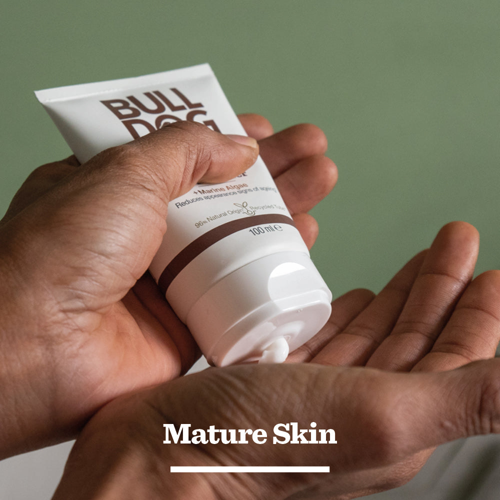A person squeezes Age Defence Moisturiser for men onto their palm, with Mature Skin written below. The green background highlights its natural origin ingredients.