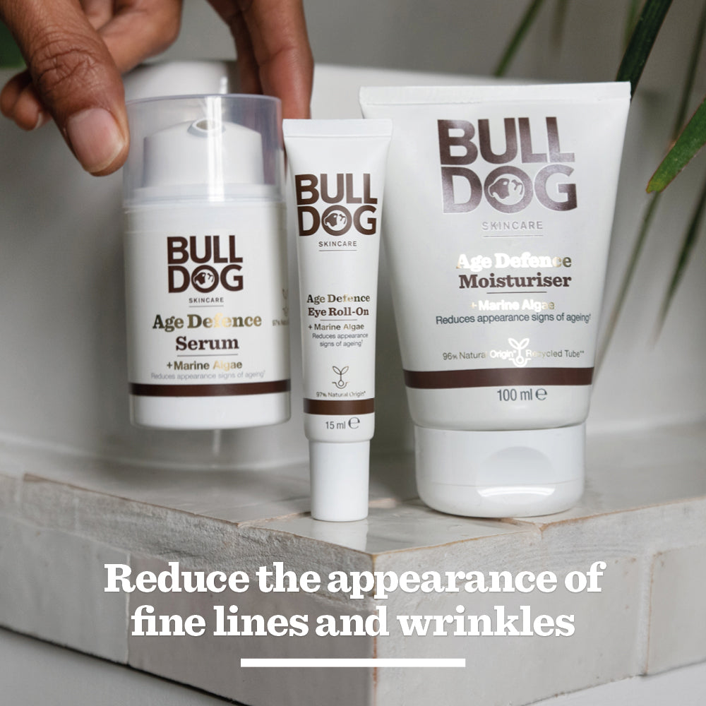 The Bulldog Skincare Age Defence Moisturiser for men is shown on a white surface with greenery in the background. Text reads: Reduce the appearance of fine lines and wrinkles.