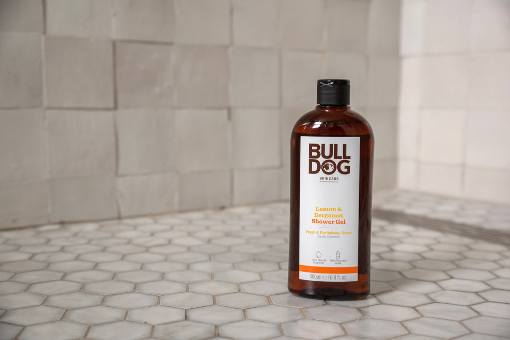 A bottle of Lemon & Bergamot Shower Gel sits on white hexagonal tiles with beige squares behind, showcasing this mens skincare essential and its refreshing, natural fragrance.