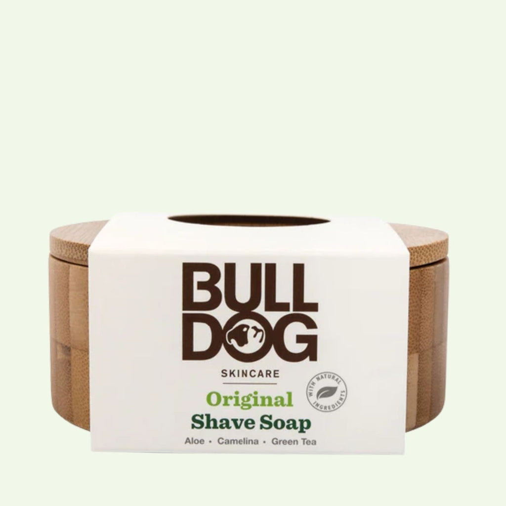 A circular wooden container featuring a white label with Original Shave Soap is shown against a pale background, highlighting its refillable design and natural origin ingredients.